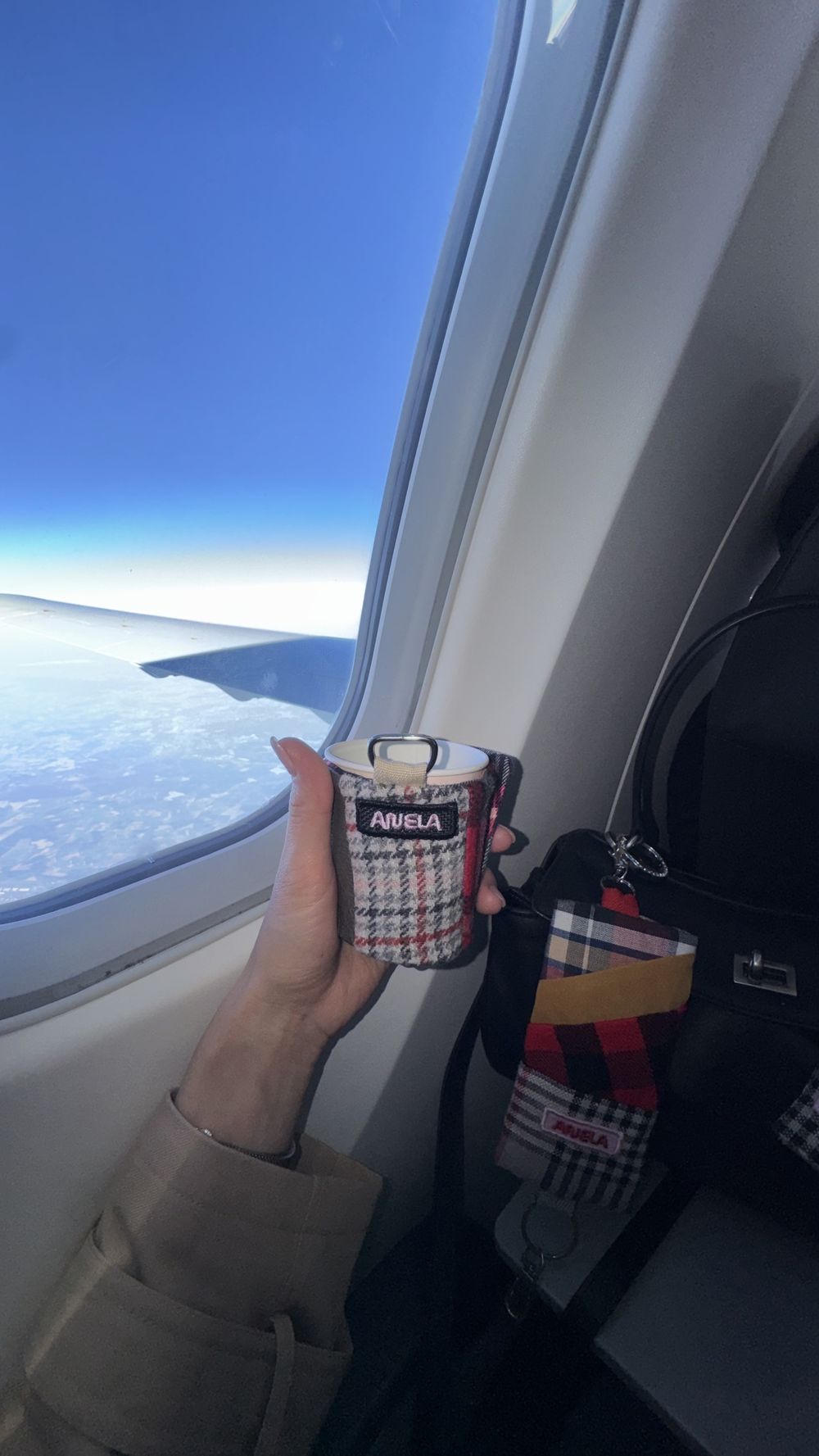 A hand holding ANELA cup holder by an airplane window